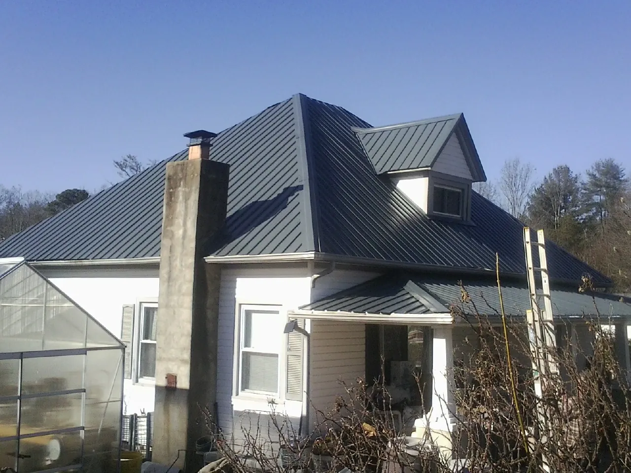 Dark blue standing seam metal roof on a white farmhouse with dormer — Slate & Tile Roof Repair by Roofing Brothers in Bessemer City