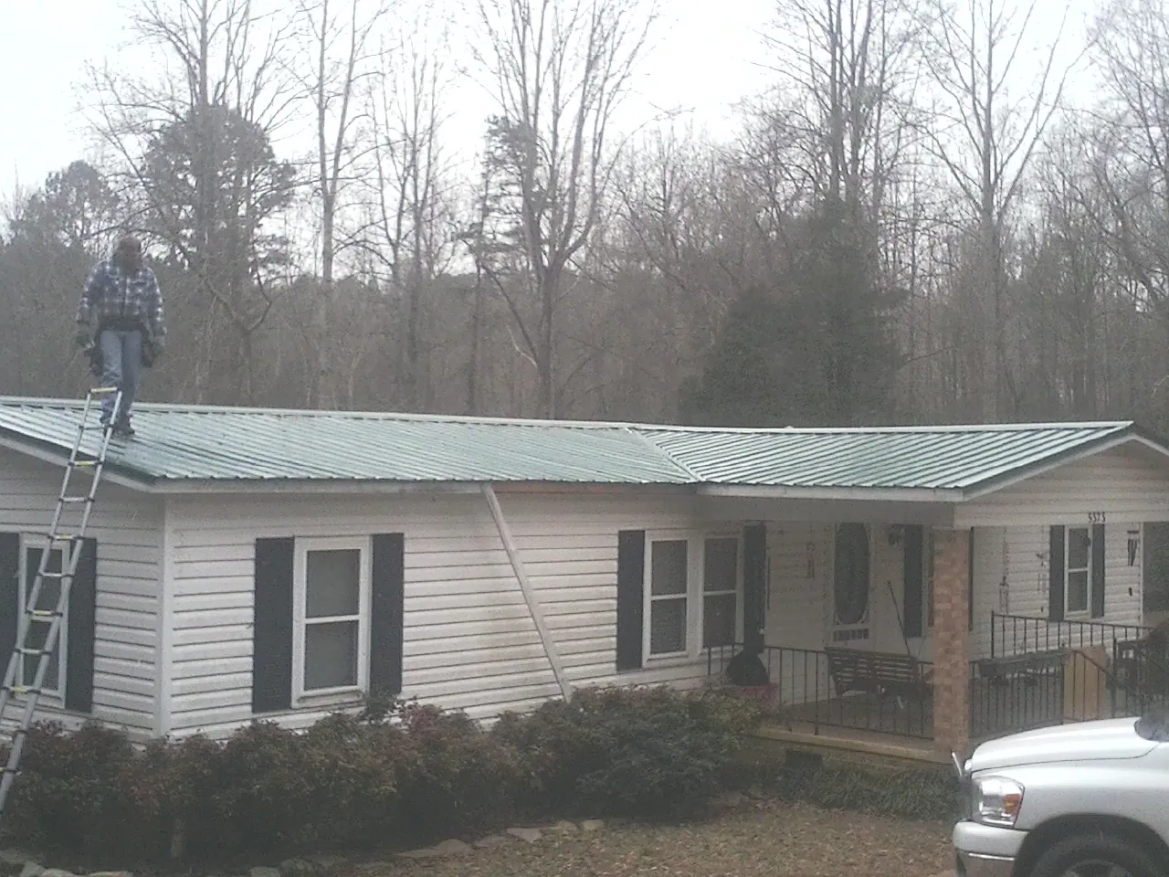 Worker on a ladder beside a new green metal roof on a ranch home in Bessemer City