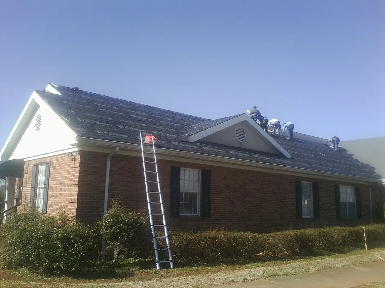 Crew tearing shingles off a brick ranch roof with a ladder set — Metal Roof Repair work by our crew in Bessemer City