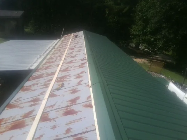 Old rusted panels beside newly installed green metal roofing — Wind Damage Roof Repair by Roofing Brothers in Bessemer City