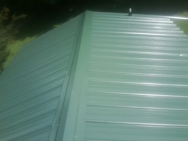 New green metal panels meeting at the ridge of a roof — Flat Roof Repair work by our crew in Bessemer City
