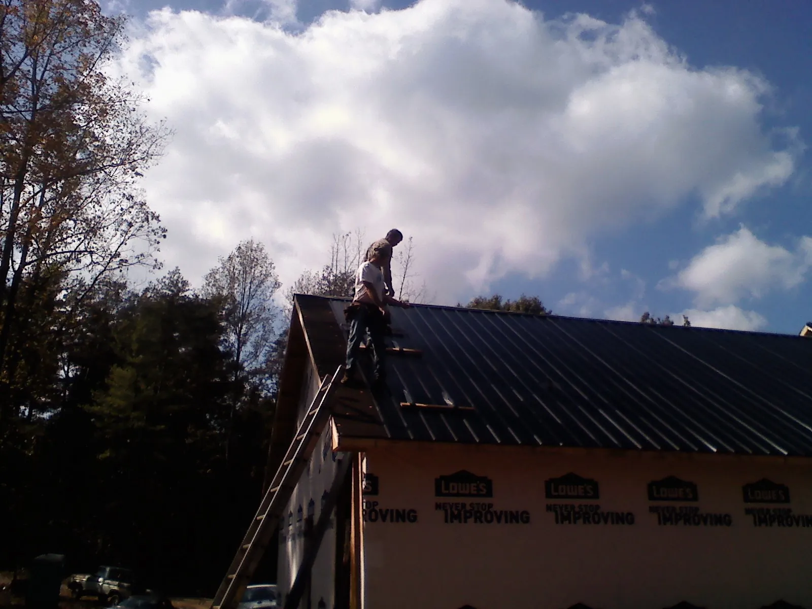 Roofer fastening dark metal panels high against a cloudy sky, from a Roof Inspection job in Bessemer City