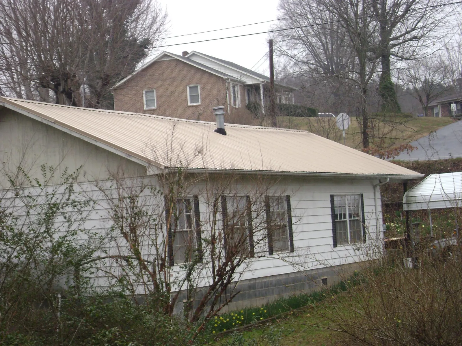 Tan metal roof on a white sided house set into a hillside — Commercial Roofing by Roofing Brothers in Bessemer City